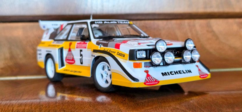 A detailed model of a rally car with distinctive white and yellow livery, featuring multiple headlights.