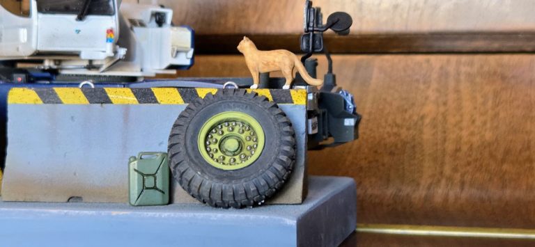 A toy cat standing on a model vehicle's wheel beside a green block.