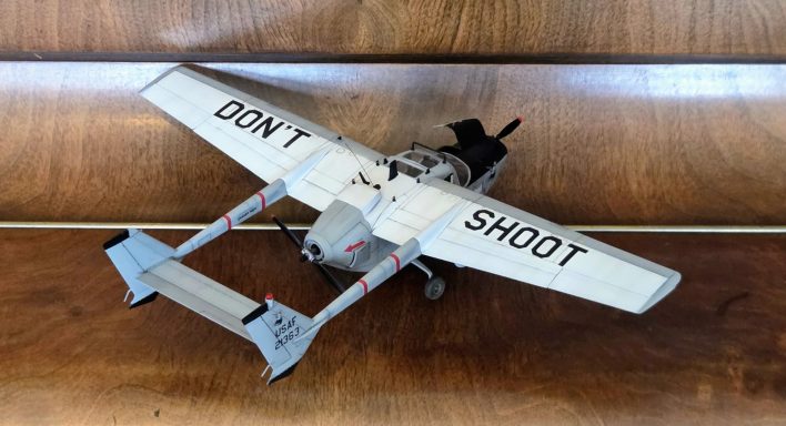 A model aircraft with the words "DON'T SHOOT" on its wings, displayed on a wooden surface.